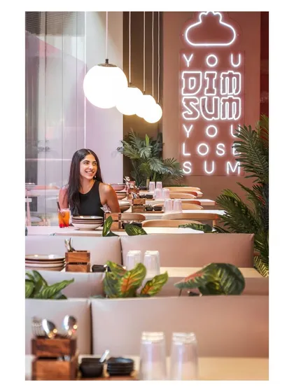 The combination of spherical pendant lights and the vertical neon sign creates a visually interesting composition. The tiered booth seating adds another layer of dimension to the space.