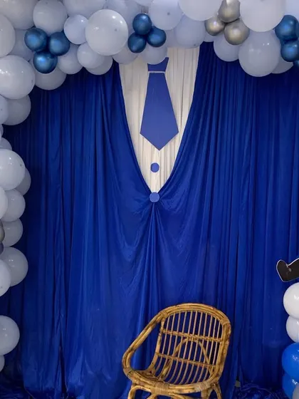 A simple yet effective 'Boss Baby' photo corner. The backdrop features a blue curtain draped to look like a suit and tie, framed by a balloon arch.
