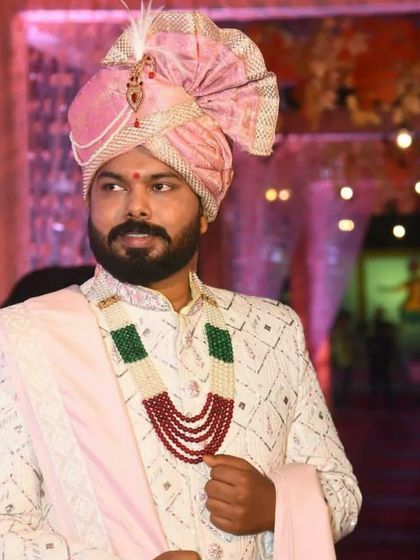 A candid shot of a groom in his wedding attire. The off-white sherwani with geometric Lakhnavi work and a contrasting pink dupatta creates a striking profile.