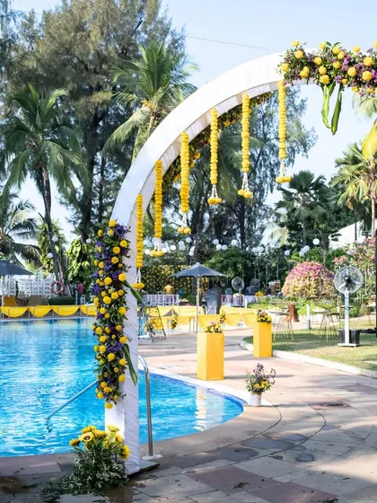 A chic poolside Haldi setup. The white floral arch with hanging marigolds beautifully frames the pool, creating a fresh and stylish ambiance for a modern Haldi ceremony.