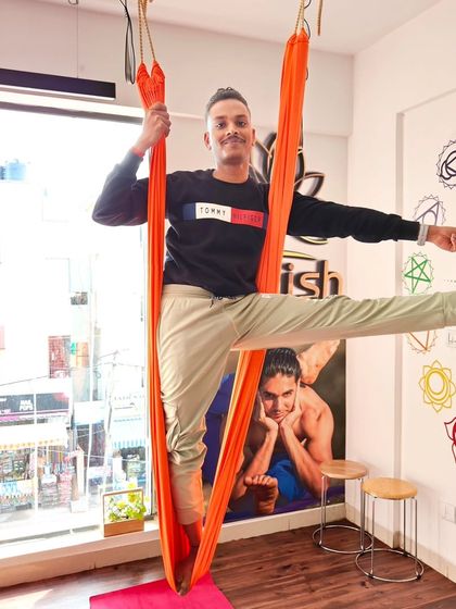 A student practices a standing balance pose with the support of the aerial hammock, perfect for improving stability.