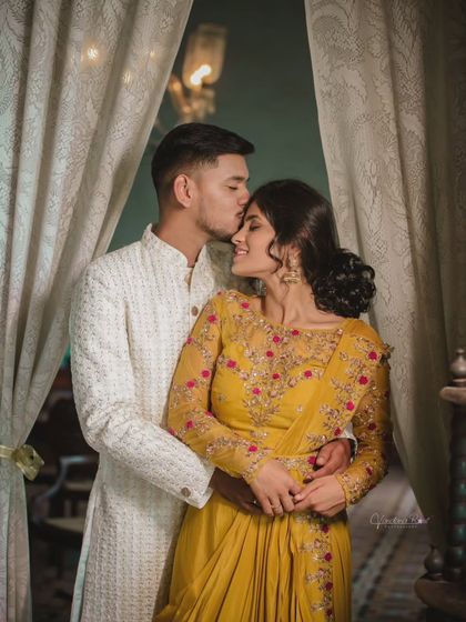 An intimate and joyful moment captured indoors. The couple's coordinated ethnic outfits in yellow and white add a bright and happy feel to this pre-wedding portrait.