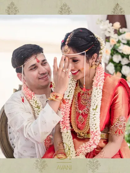 A happy couple during their wedding ceremony. The bride wears a classic red Kanchipuram saree with a custom blouse featuring unique embroidery on the arm bands.