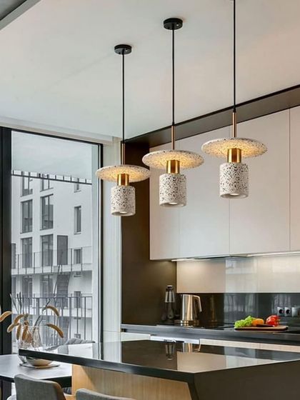 A set of three terrazzo pendants installed over a modern kitchen island. They add a touch of texture and pattern to the sleek space.