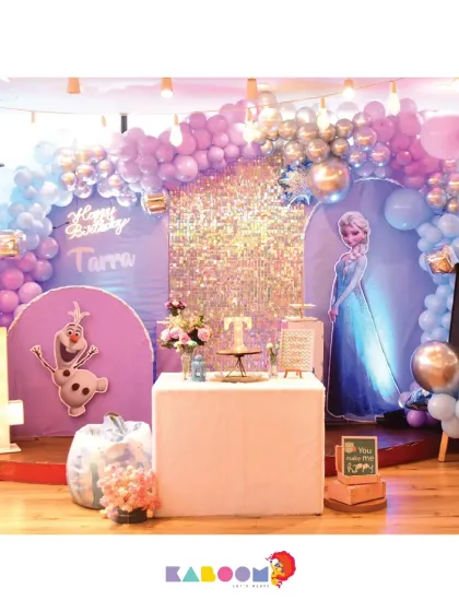 A magical Frozen-themed party for a fourth birthday, featuring a stunning balloon arch in shades of purple and blue, a sparkling backdrop, and a light-up number four.