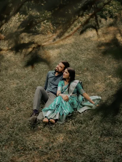 A dreamy, romantic shot of a couple relaxing on the grass. The framing through the leaves adds a touch of artistry to this peaceful pre-wedding moment.