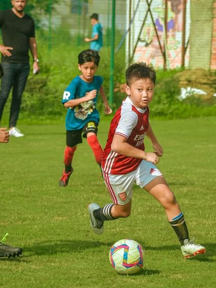 A young player in an Arsenal-style kit dribbles with speed and determination.
