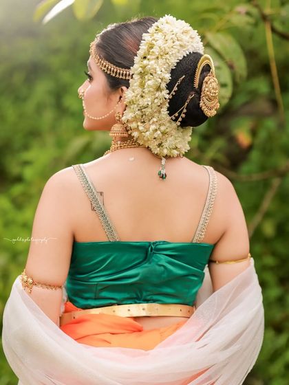 Inspired by the grandeur of Bahubali, this "Sakhi" look features a model in a unique orange and green dhoti-style saree. The outdoor setting and regal jewelry complete the ancient princess aesthetic.