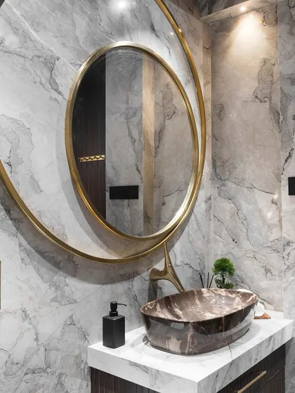 Luxury is in the details. This bathroom features a stunning gold-framed oval mirror against a grey marble wall, proving that mirrors can be the ultimate statement pieces.