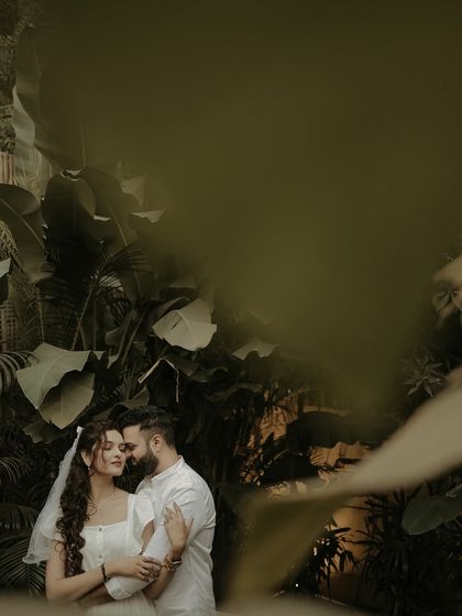 A moody and intimate portrait of a couple surrounded by lush, dark foliage. The creative framing gives the impression of a secret, stolen moment in a hidden paradise.