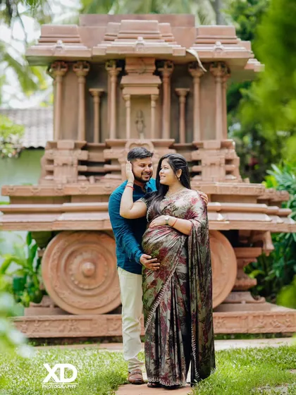 A loving pose with the partner gently caressing the mother-to-be's hair, set against the impressive stone chariot.