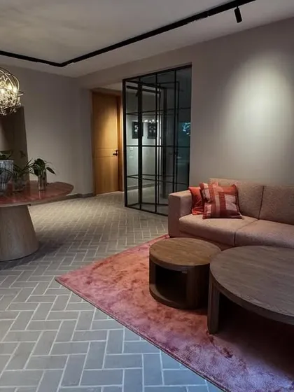 This shot captures the evening ambiance of the office lounge. The warm lighting highlights the earthy tones of the furniture and the herringbone floor, creating a cozy and sophisticated workspace.