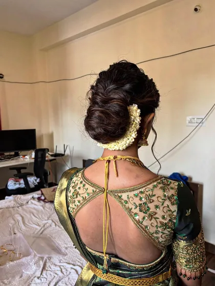 An intricate, textured low bun adorned with a classic jasmine flower 'Gajra'. This style is perfect for brides who want a sophisticated and timeless updo that stays secure through all the festivities.