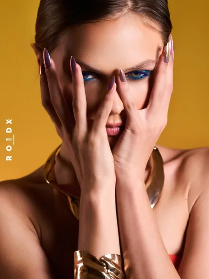 Another shot from the Roidx cover series, this pose uses the model's hands to frame her face, drawing attention to her striking eyes and long nails. The wide gold cuff and necklace remain prominent, completing the powerful, modern aesthetic.