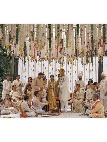 The couple and their families gathered at the mandap. The image showcases the beautiful layers of hanging flowers that create a sense of being enveloped in blooms.