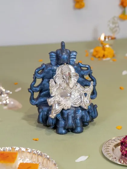 This unique Ganesha idol features a silver-plated form seated upon a throne of blue elephants. It is a powerful symbol of wisdom and strength, blending two auspicious figures into one stunning sculpture.