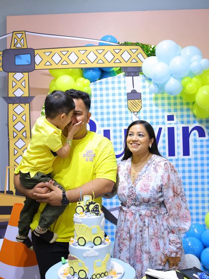 A sweet family moment as the birthday boy whispers a secret to his dad by the construction-themed cake.