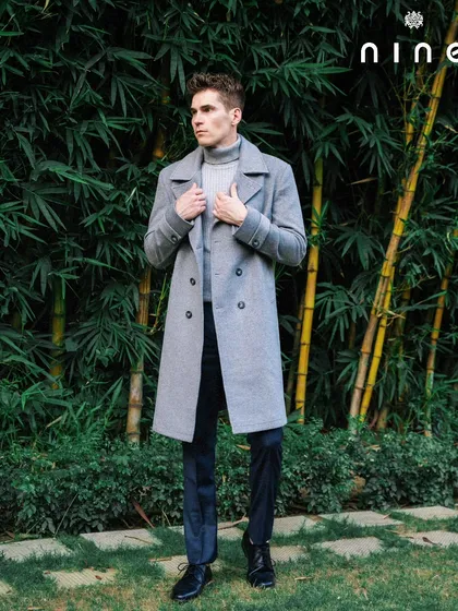 A three-quarter shot of the grey overcoat against a natural bamboo background, highlighting its clean silhouette.