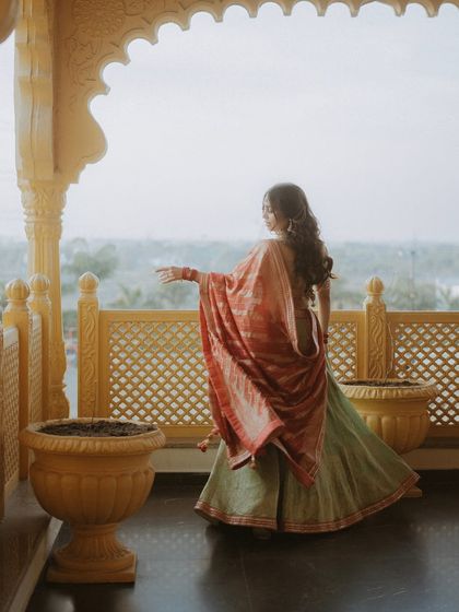 The bride looks out from a palace balcony, her colorful dupatta contrasting with the serene background.