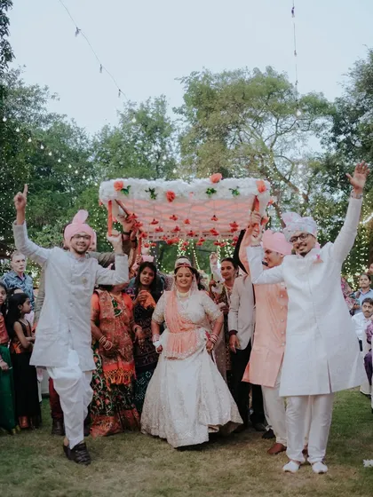 The bride's joyful entrance under a beautiful phoolon ki chaadar, surrounded by her cheering family. This is a moment of celebration and happiness.