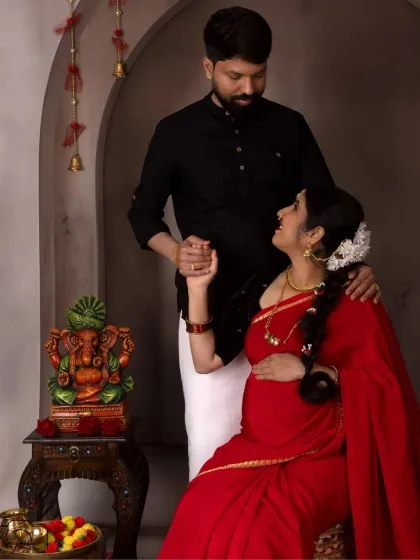 A classic seated portrait of the couple, with the Ganesha idol in the background adding a spiritual and auspicious element to their maternity photo.