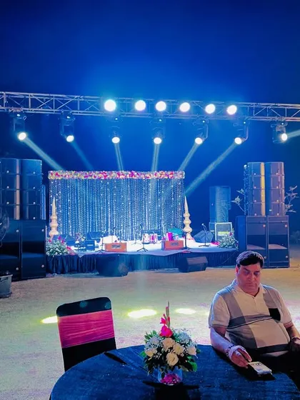 A full-scale outdoor stage setup for a sangeet or reception, complete with a professional lighting truss, moving head lights, and a powerful sound system to get the party started.