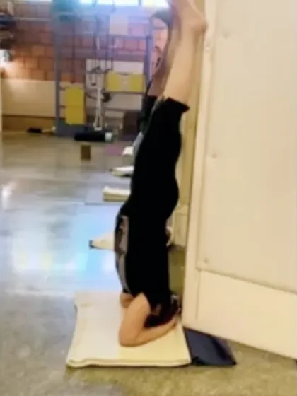 This is a Sirsasana (headstand) variation with straight legs, practiced at the corner of two walls. This setup is excellent for refining alignment and building the strength to sustain the pose for many years.