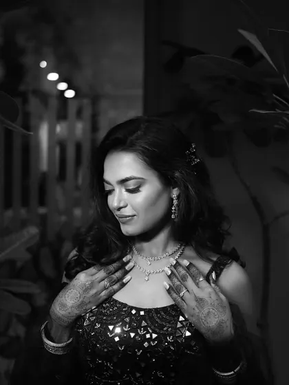 A moody black and white portrait of the bride, her hands gently touching her necklace. This image focuses on the details of her jewelry and the emotion conveyed through her serene expression.
