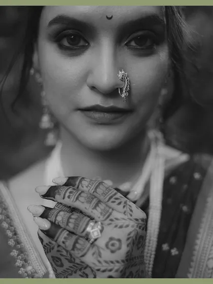 A powerful black and white portrait of a Maharashtrian bride. The focus is on her expressive eyes, traditional nath, and the intricate mehndi on her hands, creating a timeless and soulful image.