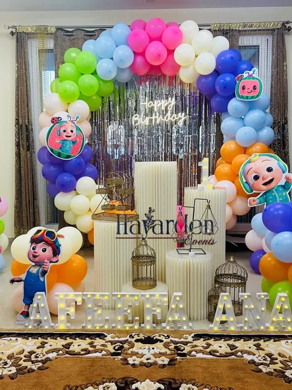 This Cocomelon setup is perfect for a home celebration. It features a colorful balloon arch against a silver fringe curtain, large character standees, and light-up marquee letters for the name.