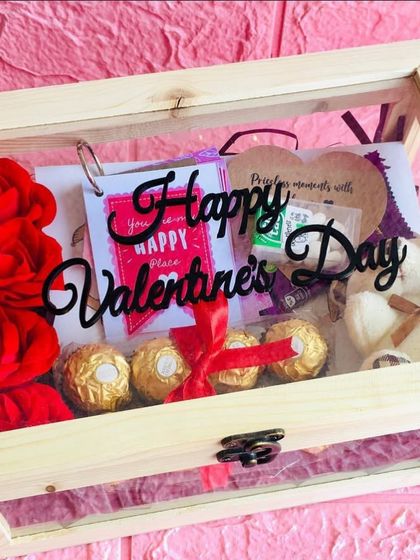 A closed view of a Valentine's Day hamper in a wooden box. The clear lid shows a glimpse of the teddy bear, roses, and chocolates waiting inside.