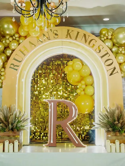 The main stage for "Ruhaan's Kingston" birthday party. A golden sequin backdrop, balloon arch, and a large initial created a glamorous focal point for the celebration.
