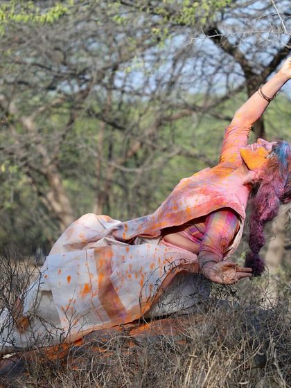 A reclining pose amidst the dry branches, covered in Holi colors. This image captures a moment of abandon and connection with the natural landscape during the spring festival.