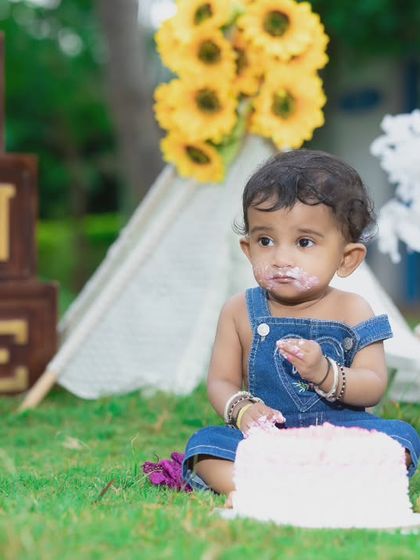 A messy but happy baby enjoying her first birthday cake in the park.