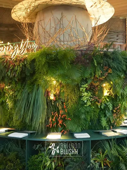 A massive, circular bar installation for home decor brand Nesterra, completely enveloped in lush, dense greenery. The brand's illuminated logo and hashtag serve as a focal point, creating an unforgettable brand activation and photo opportunity for guests.