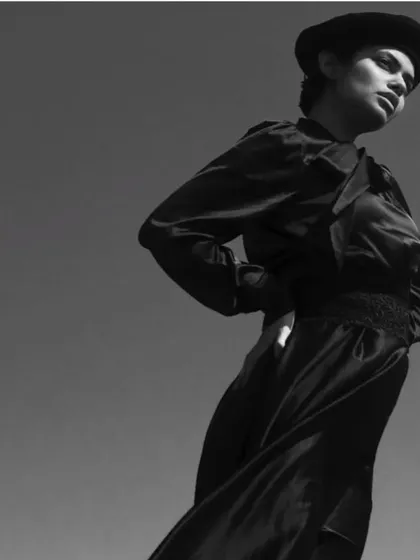 A high-fashion outdoor shoot in black and white. The makeup is clean and sculpted to stand out against the bright sky, creating a strong, graphic silhouette.