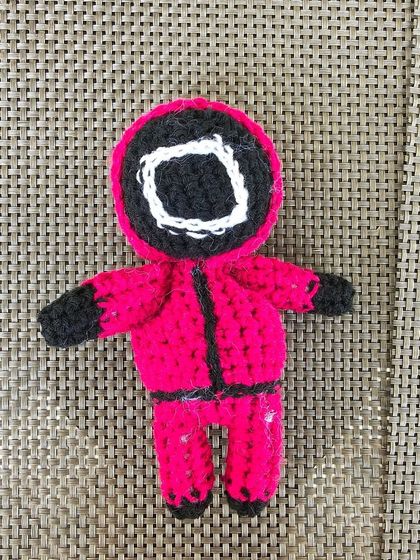 A close-up of the Squid Game guard keychain, showing the detailed stitching of the mask and uniform.