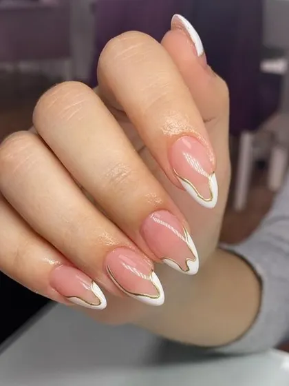 An artistic French manicure with abstract white "drips" over a nude base, outlined with a fine gold line for a touch of luxury.