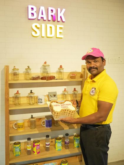 Our head chef holding a freshly made bone-shaped cake in front of our treat display. We're passionate about spreading love, one paw at a time.