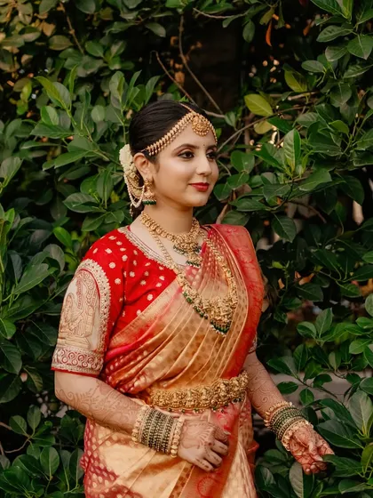 A stunning bride in her red and gold wedding saree. The makeup features classic kohl-rimmed eyes and a matte red lip, a signature look for South Indian weddings.