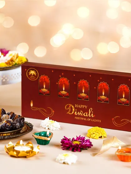 A beautifully designed Diwali gift box of dates, styled with colorful flower-shaped diyas. The warm, bokeh background adds a magical touch to this festive product shot.
