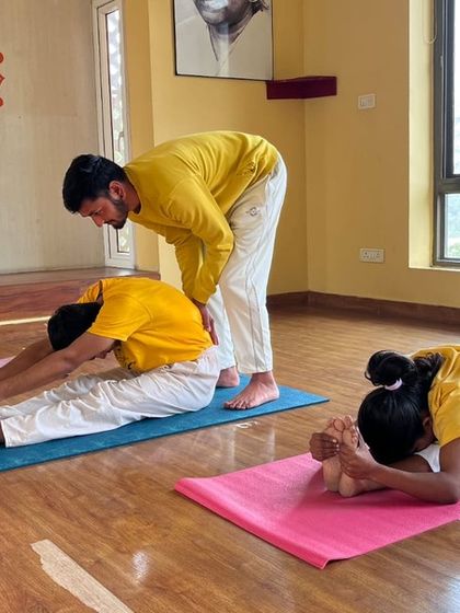 Personal attention is a cornerstone of our teaching. Here, an instructor helps students deepen their seated forward bend, offering guidance for a more beneficial stretch.