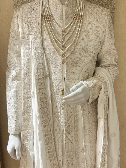Timeless elegance in a classic ivory sherwani. This piece showcases intricate self-color embroidery, paired with a matching stole and a multi-strand pearl necklace, creating a look of understated grandeur for the main ceremony.
