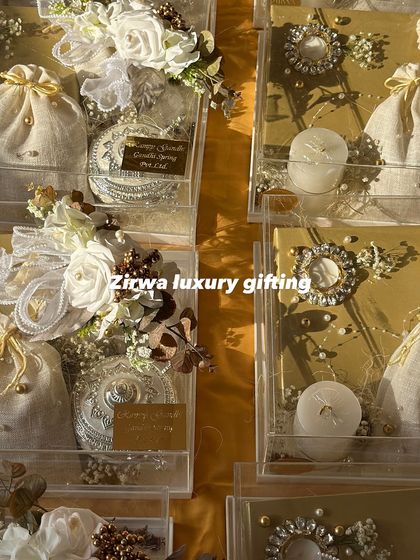 Luxurious hampers in acrylic boxes with a white and gold theme, featuring candles, potlis, and ornate silver containers.