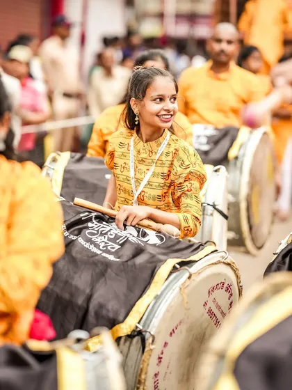 A smiling female dhol player, her happiness evident as she participates in the vibrant street festival.