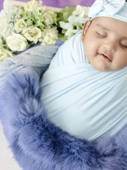 A sleepy smile from a newborn swaddled in baby blue. Nestled in a basket with a fluffy blue trim and white roses, this photo is the picture of peaceful innocence.