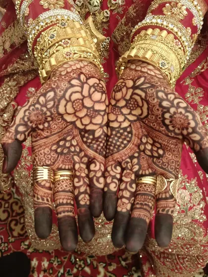 A classic bridal look with heavy gold bangles. The bold floral design on the palm stands out beautifully, showing how my henna work complements traditional wedding attire.