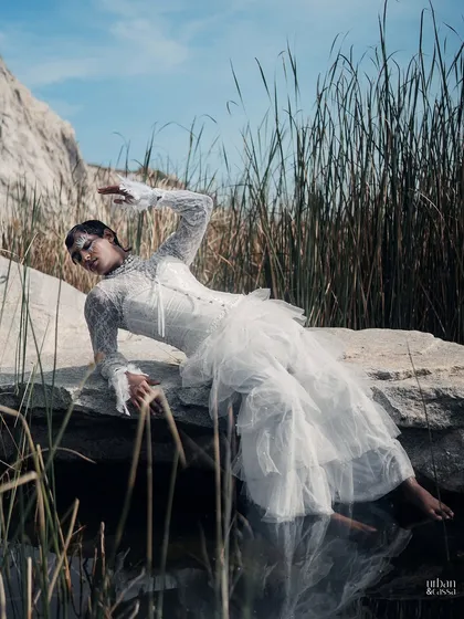 A stunning shot by the water, where the model's reflection adds another dimension to the ethereal, feather-adorned look.