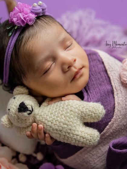 Cuddled with a tiny teddy bear, this baby girl dreams among shades of purple and pink. Using props like stuffed animals adds a touch of sweetness to the portraits.
