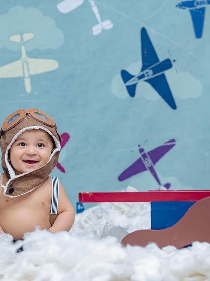 A happy little pilot flashes a big smile for the camera, showcasing the fun and imaginative 'Aviator' theme available for sitter sessions.